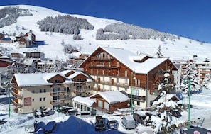 A snow-covered resort with multiple wooden buildings, including a hotel with balconies and a parking area. - Resort center, swimming pool, tv, ski locker, 38m², Les 2 Alpes (Les Deux Alpes)