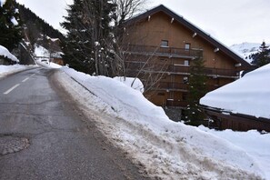 A wooden building with multiple balconies, a snow-covered road, and a mountainous backdrop. - 150m from resort center, 3rd floor, balcony, ski locker, 40m², Méribel (Méribel - Les Allues)