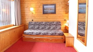 Una habitación acogedora con pared de madera, una cama con ropa de cama estampada, una mesita de noche pequeña con una lámpara y un cuadro enmarcado con una vista urbana.