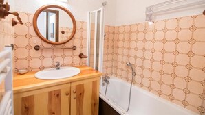 A bathroom with a wooden vanity, a round mirror, a bathtub, and patterned tiles.