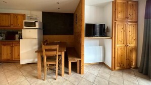 Eine kleine Küche mit Holzausstattung, einer Mikrowelle, einem Kühlschrank und einem Esstisch mit Stühlen.