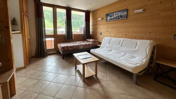 Ein gemütliches Zimmer mit einer Couch, einem kleinen Tisch und einem Bett. Es gibt ein Fenster mit Vorhängen, eine Holzvertäfelung und ein Bild an der Wand.