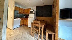 Eine kompakte Küche mit Holdekor-Schränken, einem weißen Kühlschrank, einer Mikrowelle und einem Essbereich mit Holztisch und Stühlen.
