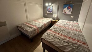 Ein Zimmer mit zwei Einzelbetten, einem Nachttisch mit Lampe und einem an der Wand befestigten Regal mit einem Bild.