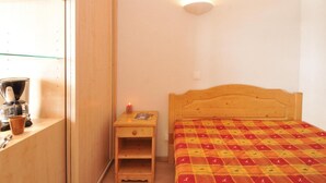 Une chambre à coucher avec un lit en bois, une table de chevet sur laquelle se trouve un livre, une machine à café et une lampe fixée au mur.