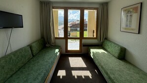 Ein Zimmer mit zwei grünen Sofas, einem Flachbildfernseher, einem Fenster mit Vorhängen und einem gerahmten Bild an der Wand.