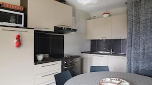 A compact kitchen with a microwave, stove, oven, and sink. There are cabinets, a chair, and a table with a basket on it. - 20m from ski slopes, Ground floor, view ski slopes, tv, 40m², La Plagne (La Plagne)