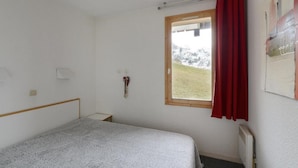 A small, simple bedroom with a single bed, a window with a view of a snowy landscape, and a radiator on the wall. - 20m from ski slopes, Ground floor, view ski slopes, tv, 40m², La Plagne (La Plagne)