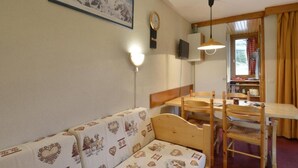 Una habitación acogedora con un sofá de madera, una mesa de comedor con sillas, un reloj en la pared y un cuadro enmarcado sobre el sofá.