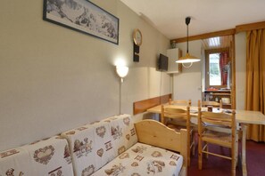 A cozy room with a wooden sofa, a dining table with chairs, a wall-mounted clock, and a framed picture above the sofa. - Ski-in/ski-out & foot of the slopes, 7th floor, view ski slopes/ski slopes, balcony, tv, 28m² (La Plagne)