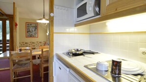 Cocina pequeña con gabinetes blancos, un microondas, estufa y lavamanos. Cuenta con una mesa de comedor con sillas y una lámpara colgante.