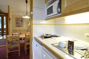 A compact kitchen with white cabinets, a microwave, a stove, and a sink. There is a dining table with chairs and a hanging light fixture. - Ski-in/ski-out & foot of the slopes, 7th floor, view ski slopes/ski slopes, balcony, tv, 28m² (La Plagne)