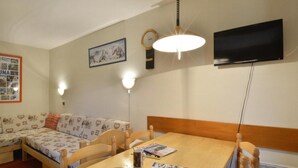 Una habitación acogedora con una mesa de comedor de madera, un sofá y un televisor montado en la pared.