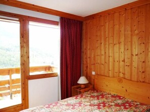 A room with a bed, a window with curtains, a wooden headboard, and a nightstand with a lamp.