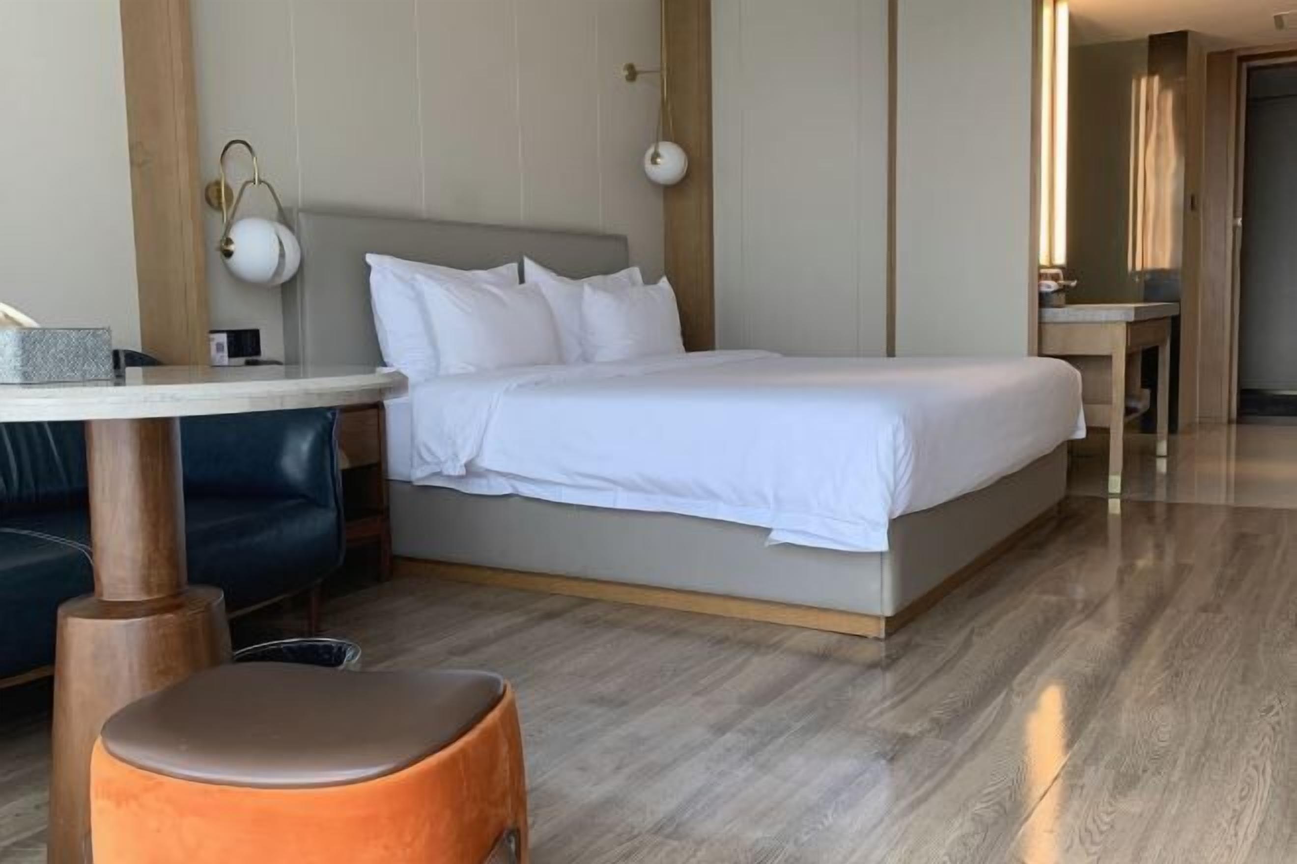 A hotel room with a bed, a small table, a sofa, and a wooden floor.