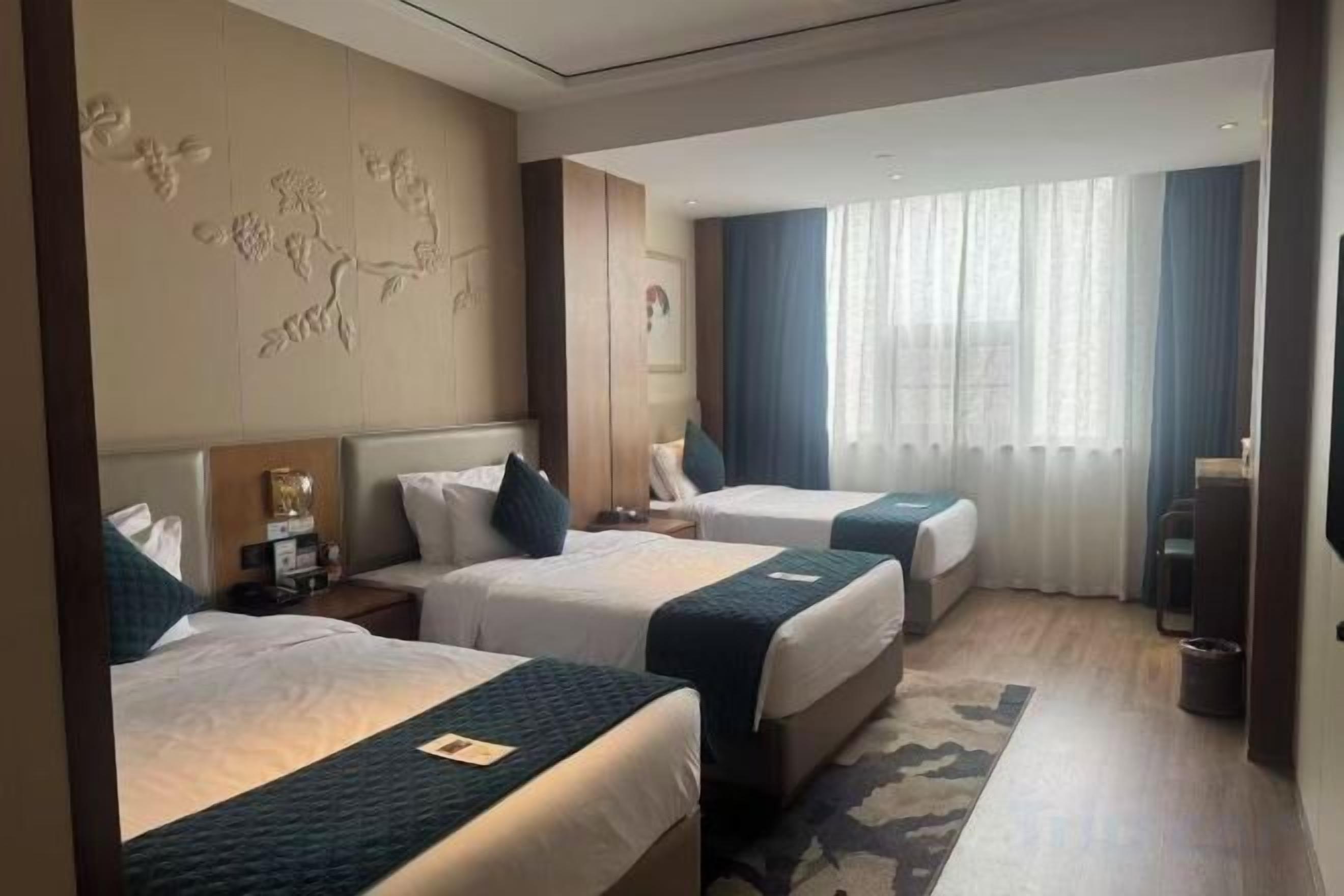 A hotel room with two beds, a desk, and a large window with curtains.