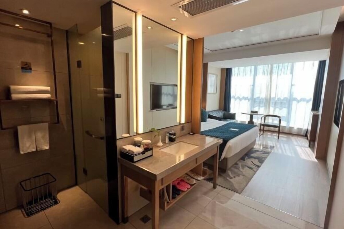 A modern hotel room with a large mirror, a bed, a TV, and a bathroom with a shower and a towel rack.