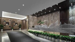 A modern reception area with a marble counter, potted plants, and a dark reception desk. - Xiangtan Manqi Hotel (Xiangtan)