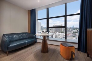 Una habitación moderna con un sofá de cuero, una mesa redonda de madera y vistas de la ciudad a través de amplias ventanas.