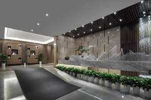 A modern reception area with a marble counter, plants, and a black carpet. - Xiangtan Manqi Hotel (Xiangtan)