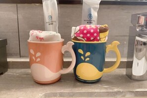 Two mugs with unique designs, one orange and one blue, placed on a countertop. - Xiangtan Manqi Hotel (Xiangtan)