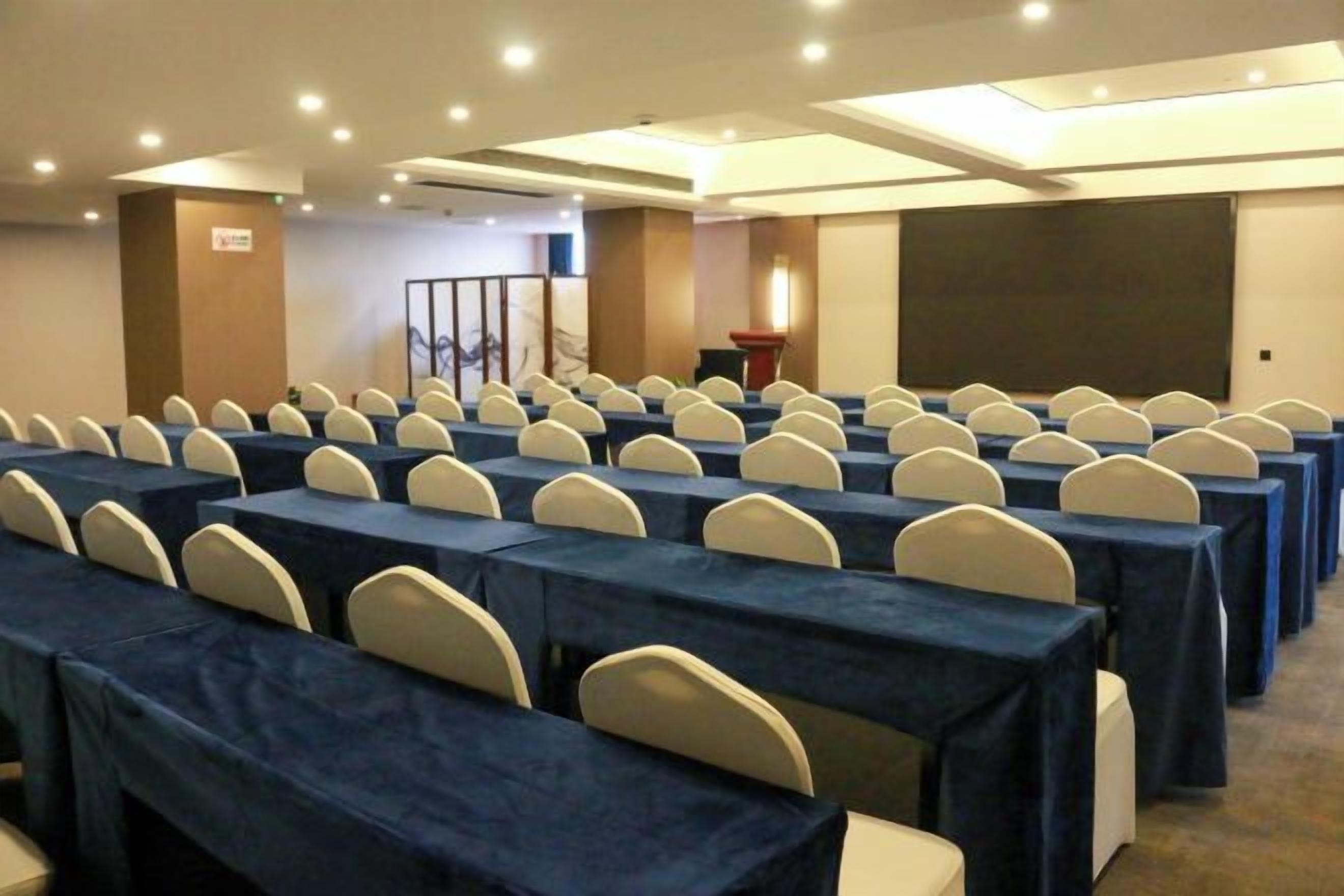 A conference room with rows of tables and chairs, a podium, and a projection screen.