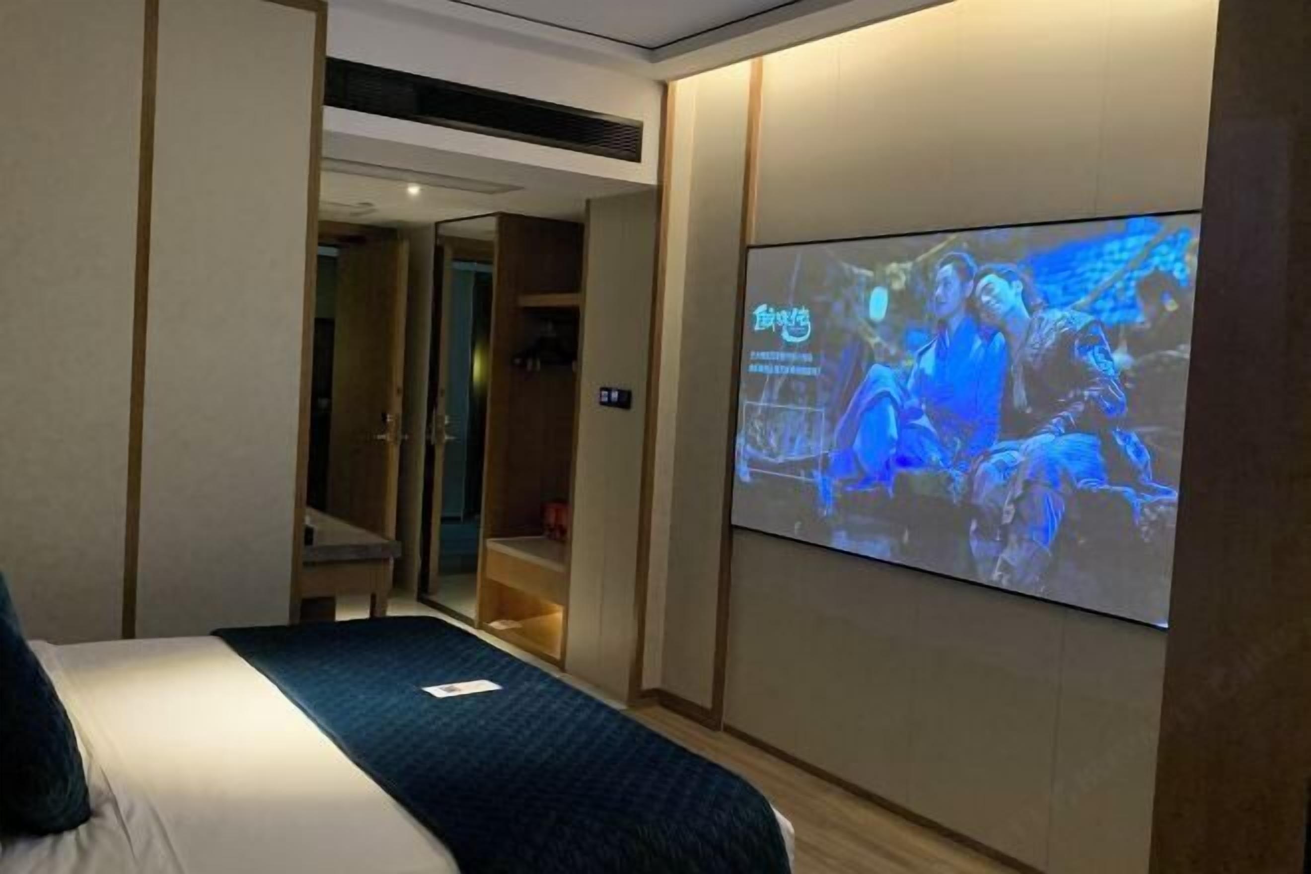 A hotel room with a bed, a TV screen displaying a movie, and a wooden wardrobe.