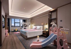 A hotel room with a bed, a desk, a chair, a small table, a bookshelf, a window, and a children's play area. - Xiangtan Manqi Hotel (Xiangtan)