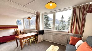 A cozy room with a sofa, a wooden table, a TV, and a window with curtains.