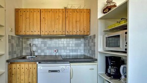 A compact kitchen with wooden cabinets, a dishwasher, a microwave, and a coffee maker.