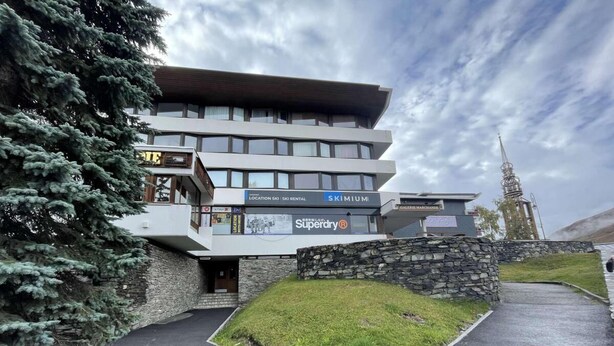 A modern building with a ski rental sign, stone walls, and a grassy area in front.