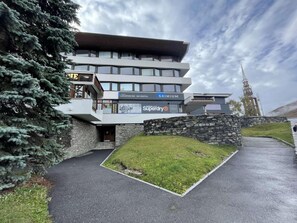 A modern building with a ski rental sign, stone walls, and a grassy area in front. - 10m from ski slopes, 1st floor, tv, ski locker, 24m², Les Menuires (Les Menuires)