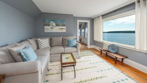Un salon comprenant un canapé, une table basse, un banc et une grande fenêtre donnant sur un lac.