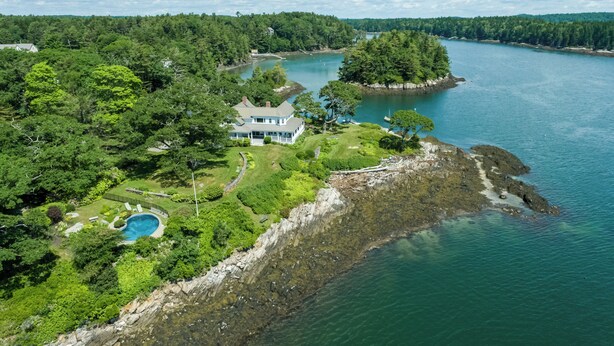 Vue aérienne d’une propriété située sur la côte, avec une grande maison, une piscine et une plage rocheuse.