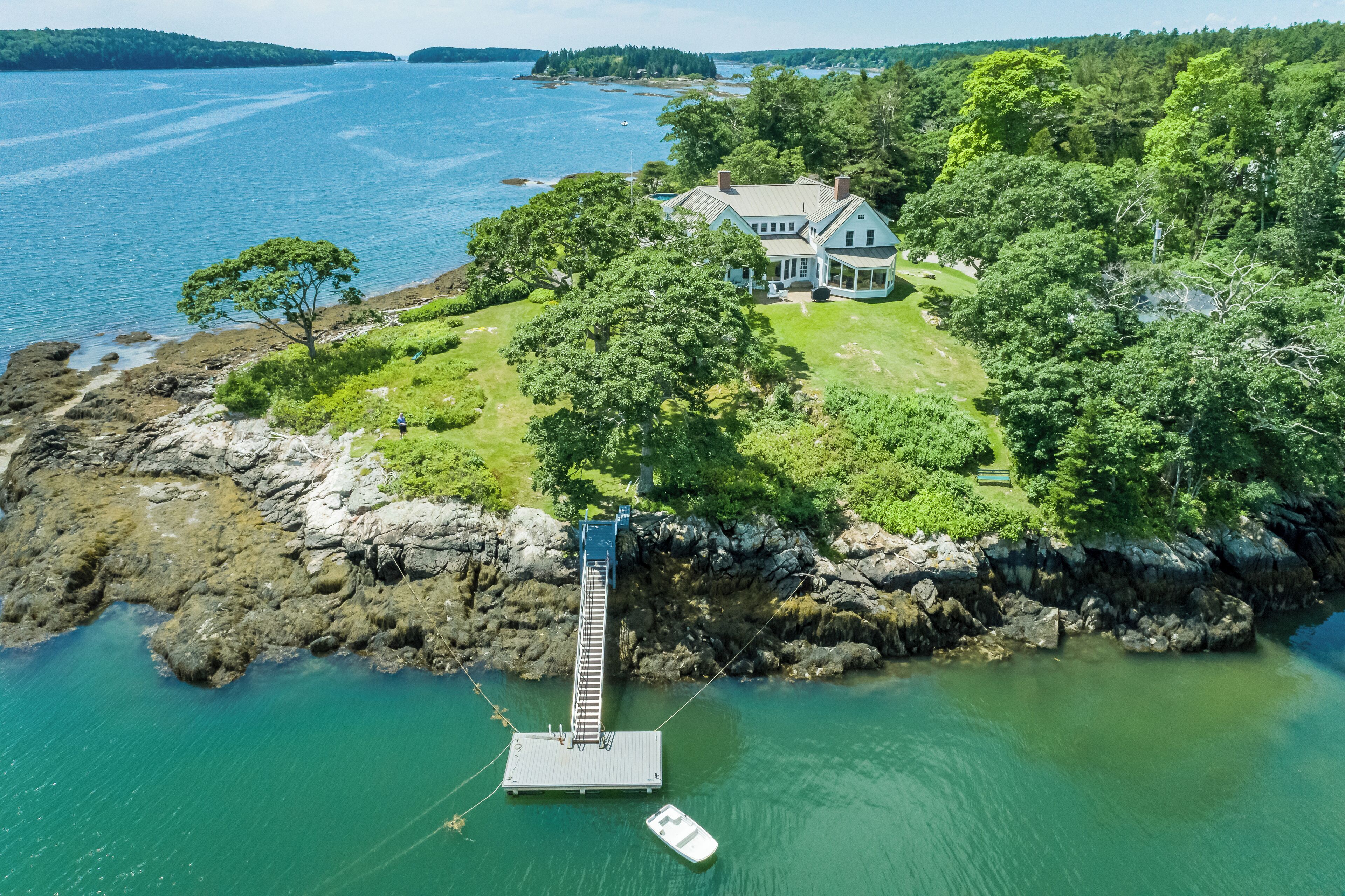 A coastal property with a dock, a house surrounded by trees, and a view of the sea.