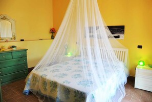 A bedroom with a canopy bed, a dresser, a nightstand, a mirror, and a wall-mounted picture.