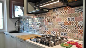 A kitchen with a patterned backsplash, a gas stove, and a window. - VILLA CORBEZZOLO between nature and the sea (Sperlonga)