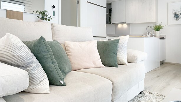 Een moderne woonkamer met een beige bank, een keuken met witte kasten en een klein keukeneiland met een spoelbak.