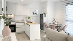 Een moderne keuken met witte kasten, een centraal eiland en een eetgedeelte met een glazen tafel en stoelen.