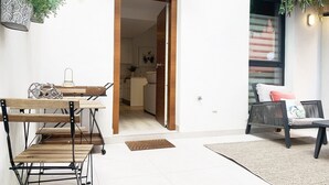 Een moderne woonruimte met een eethoek, een zithoek met een bank en kussens, en een keuken die door een open deur zichtbaar is.