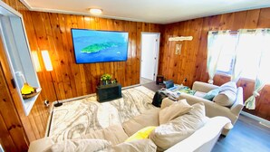 Una sala de estar acogedora con un televisor de pantalla plana grande montado en la pared, un sofá cómodo, una mesita con una planta y piso de madera.