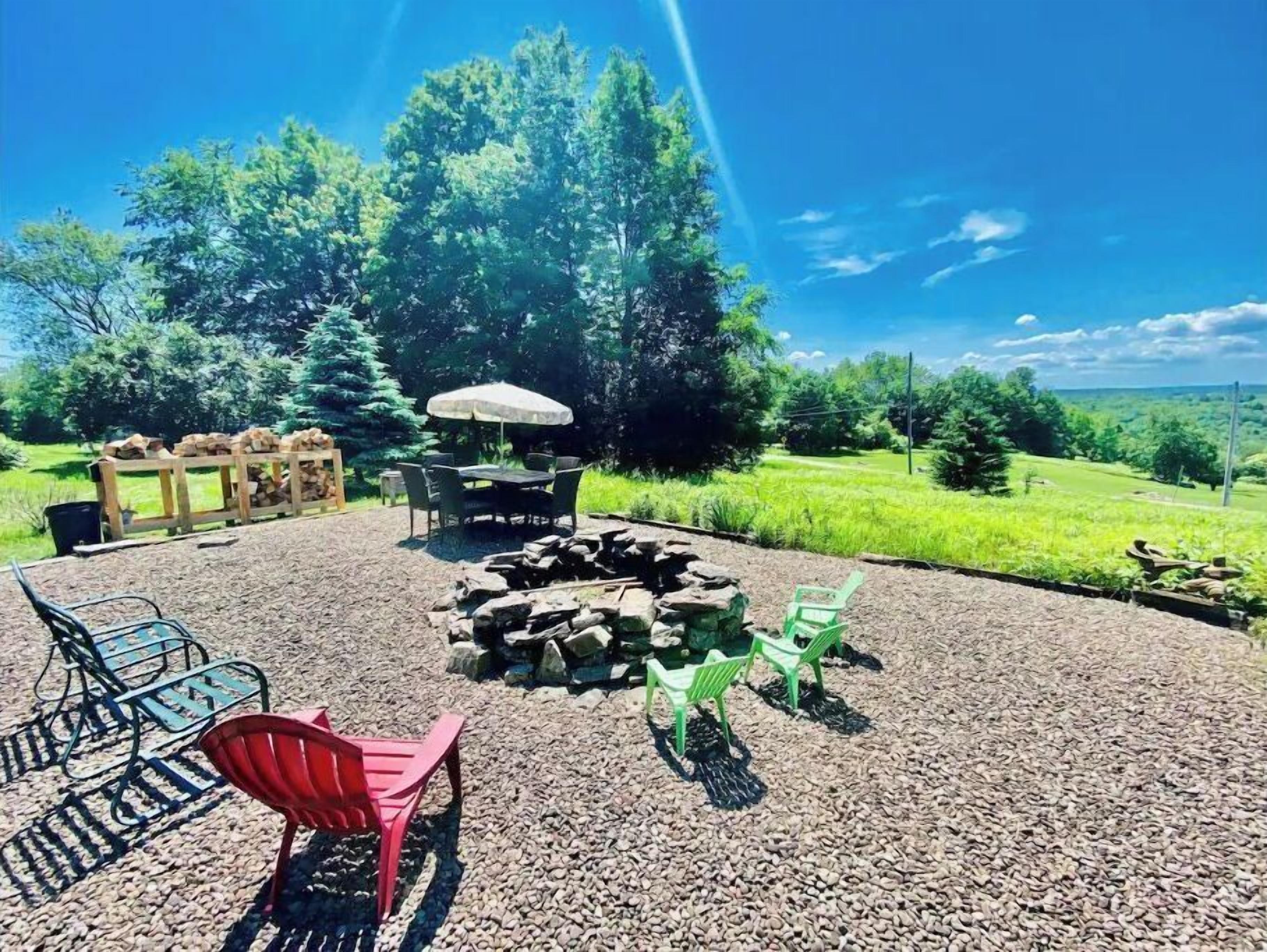 An outdoor seating area with a fire pit, chairs, and a table under a canopy.