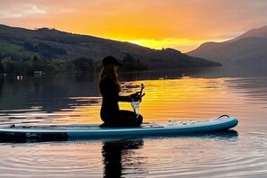 Une personne assise sur une planche à pagaie, sur une étendue d’eau calme, avec un coucher de soleil en arrière-plan.