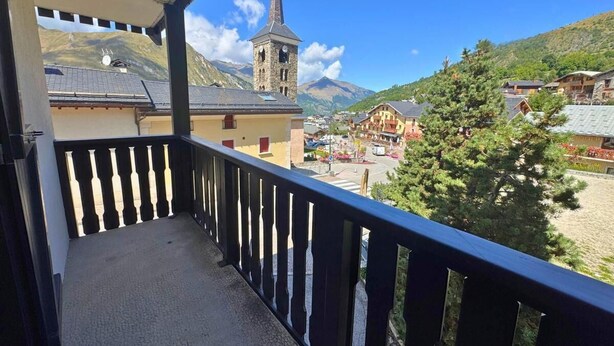 Un balcón con vistas a un pueblo, una torre de iglesia y montañas.