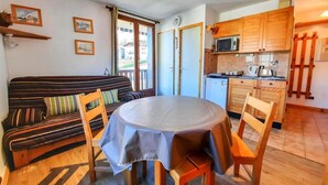 Una habitación acogedora con una mesa redonda, sillas de madera, un sofá y una zona de cocina con armarios de madera y un microondas.