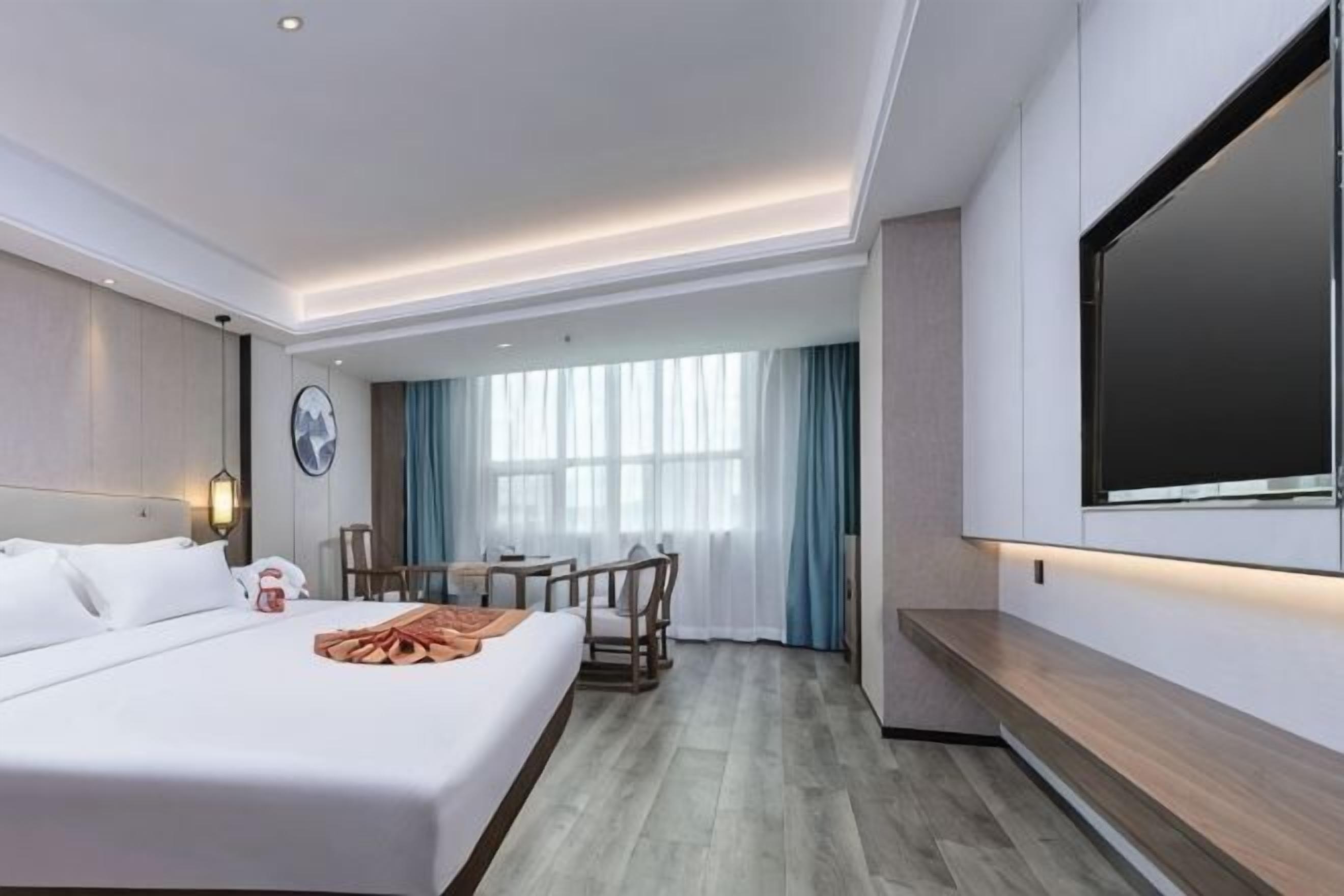 A hotel room with a bed, a desk, a chair, a TV, and a window with curtains.