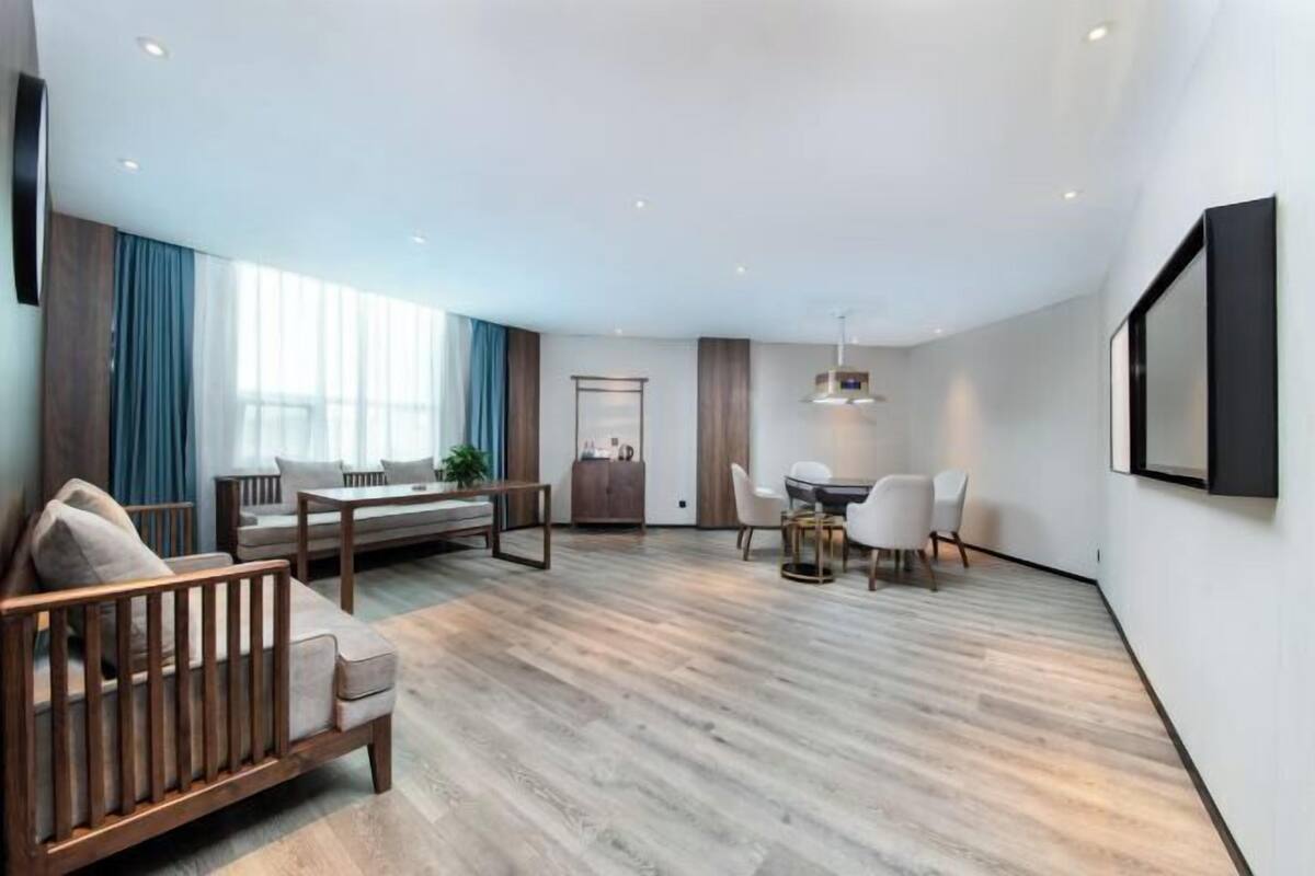 A modern living room with a sofa, a dining table with chairs, and a kitchen area with a refrigerator.