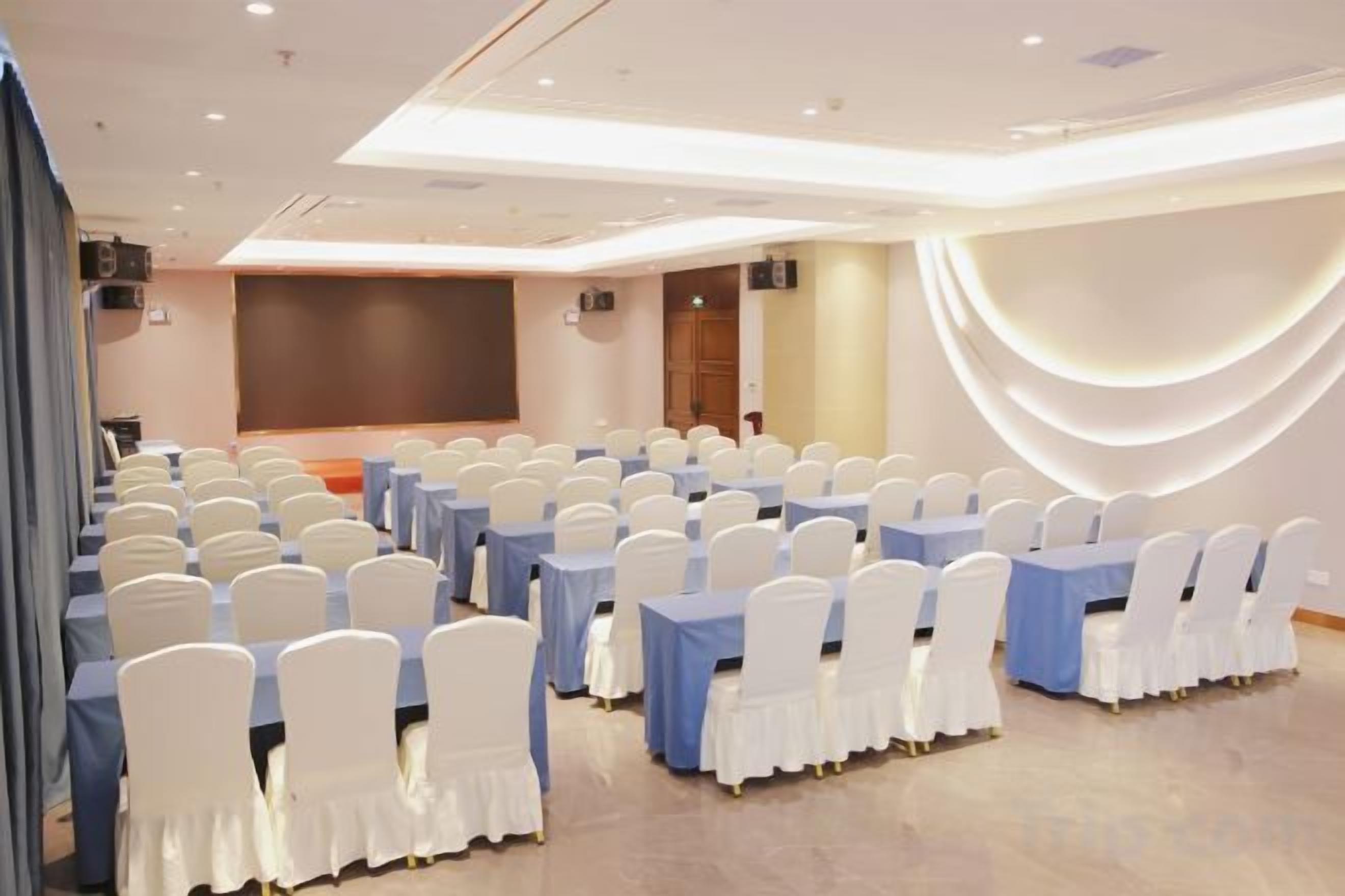 A conference room with rows of white chairs, blue tables, and a stage.