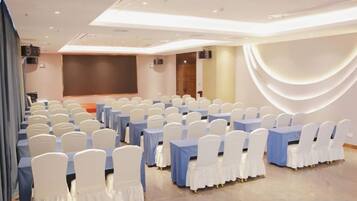 A conference room with rows of white chairs, blue tables, and a stage.