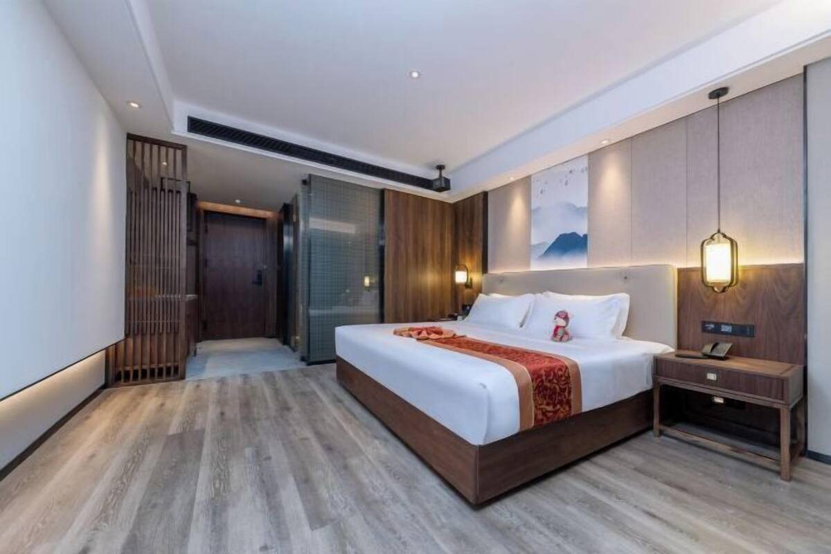 A modern hotel room with a large bed, a bedside table, a wall-mounted lamp, and a sliding door leading to a bathroom.